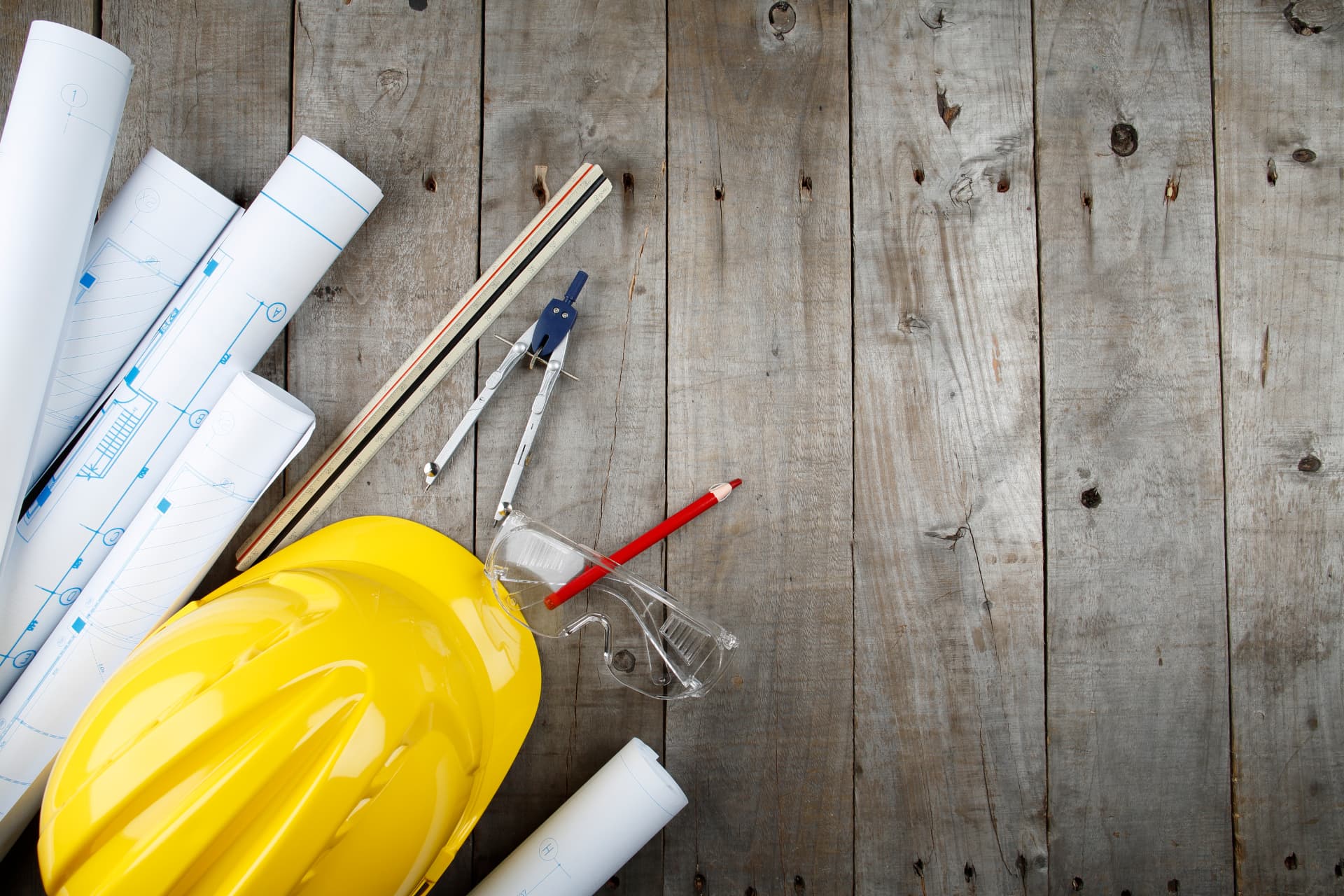 Blueprints, a hard hat and drafting tools on a workbench